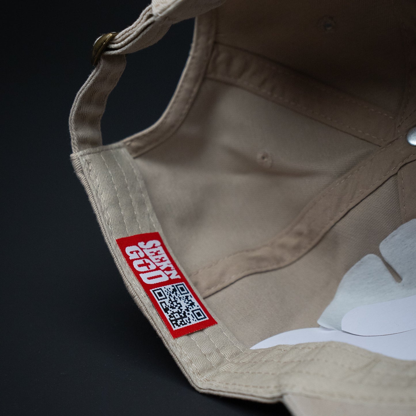 Beige cap with a red label featuring a QR code on a dark background