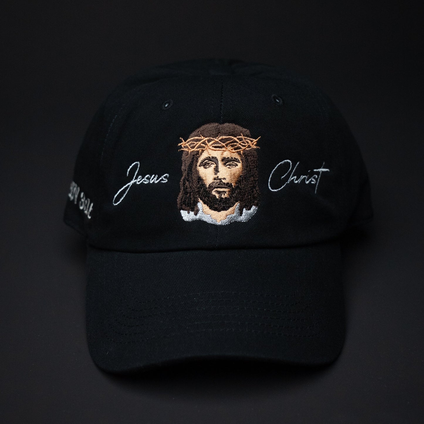 Black cap with embroidered face of Jesus and text on a black background