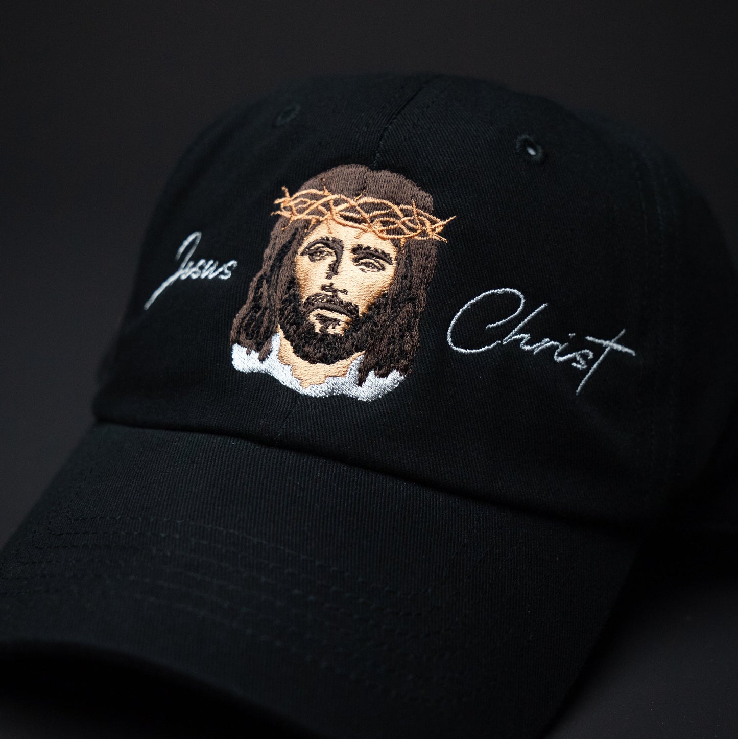 Black cap with embroidered image of Jesus Christ and 'Jesus Christ' text on a dark background