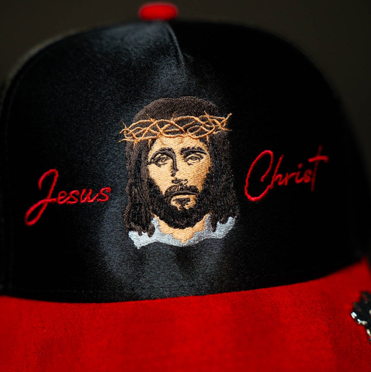 Black and red cap with embroidered face and 'Jesus Christ' text on a dark background