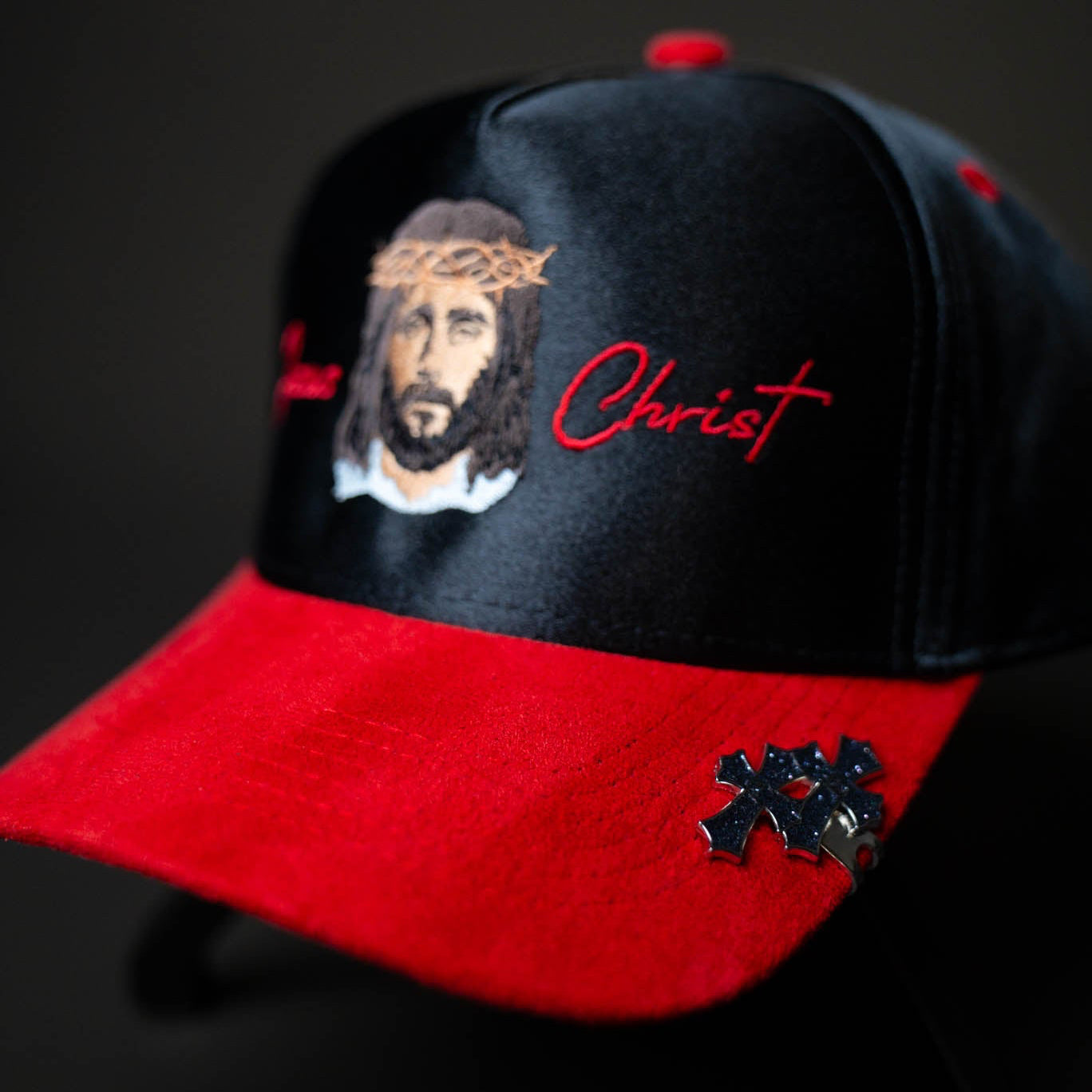 Black and red cap with an embroidered face and 'Christ' text on a dark background
